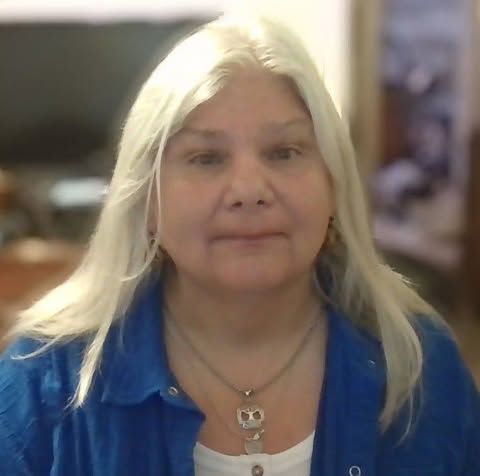 Portrait of a woman with long blond hair wearing a blue shirt and necklace, indoors.
