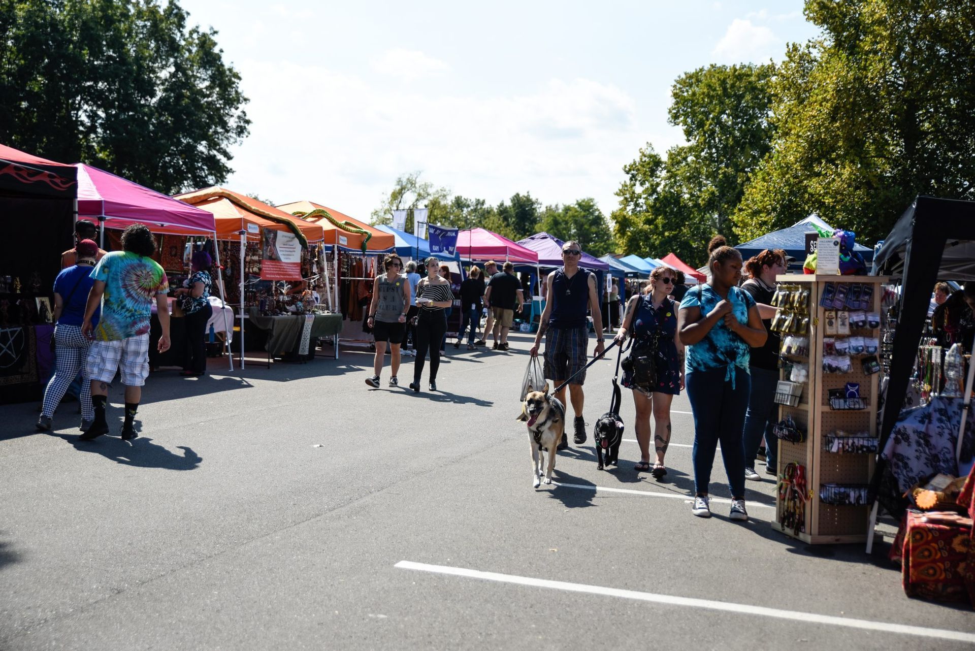 Outdoor market with colorful tents, people walking, and a cyclist on a sunny street