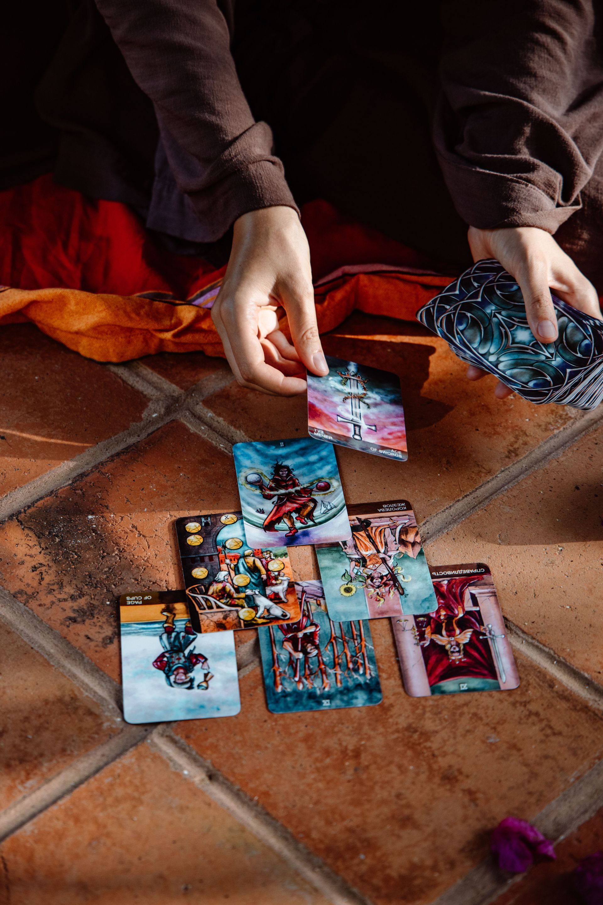 Hands arranging colorful trading cards on a tiled floor with a red blanket nearby