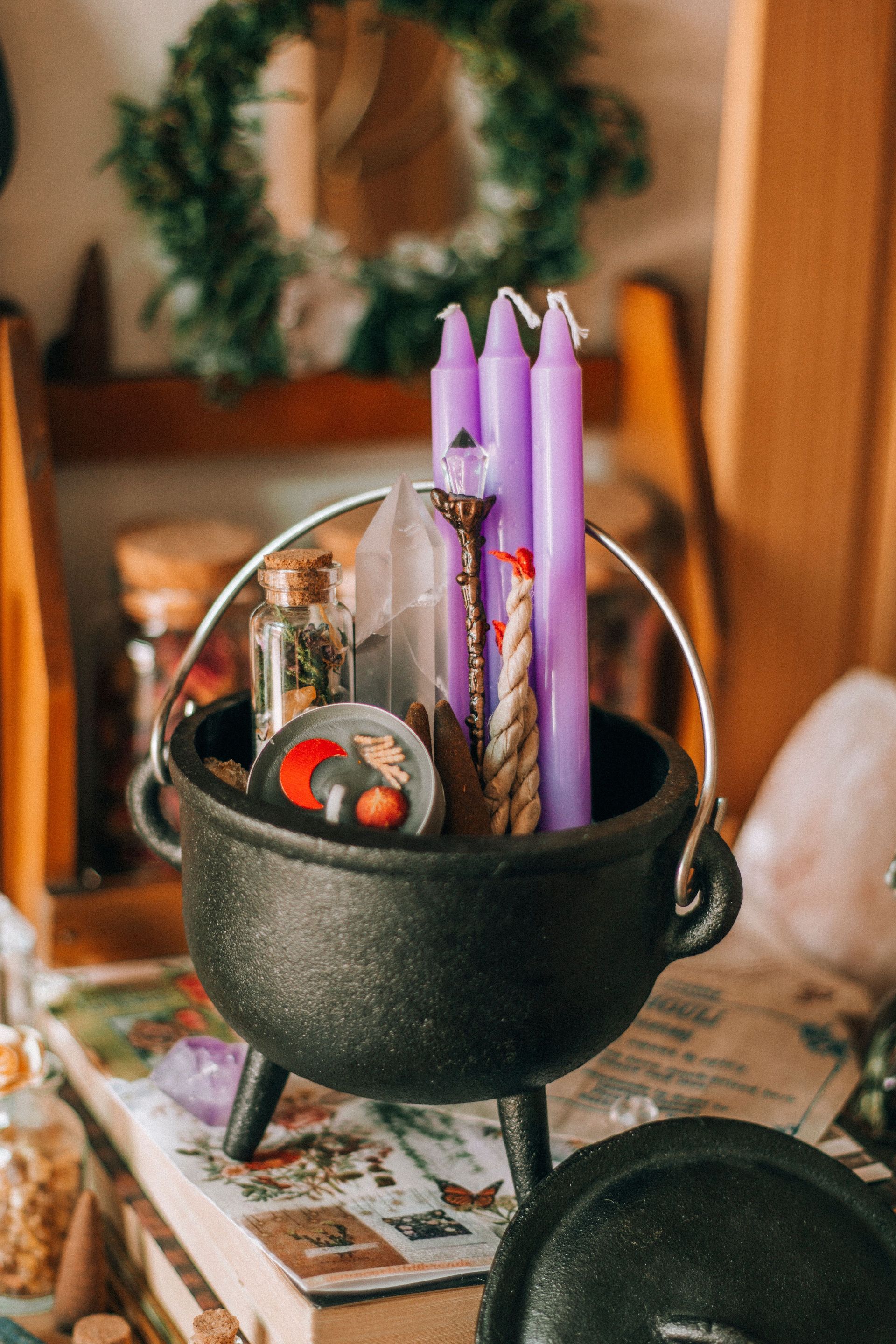 Black cauldron holding purple candles and witchy trinkets on a tabletop with autumn decor