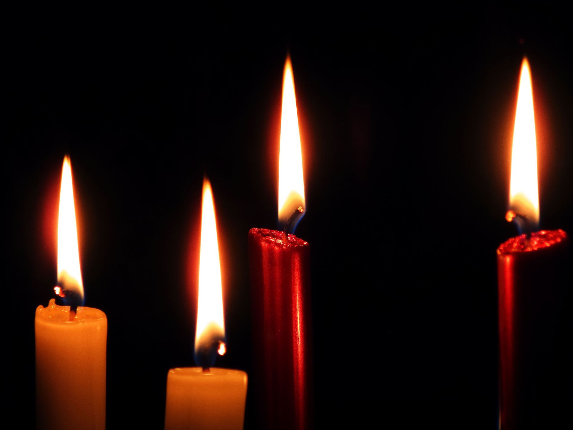 Four lit candles on a dark background, two orange and two red, with glowing flames.