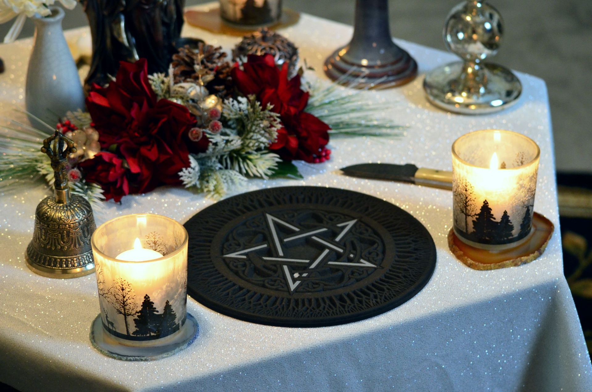 Pagan altar with lit candles, pentagram centerpiece, and red flowers on a white cloth
