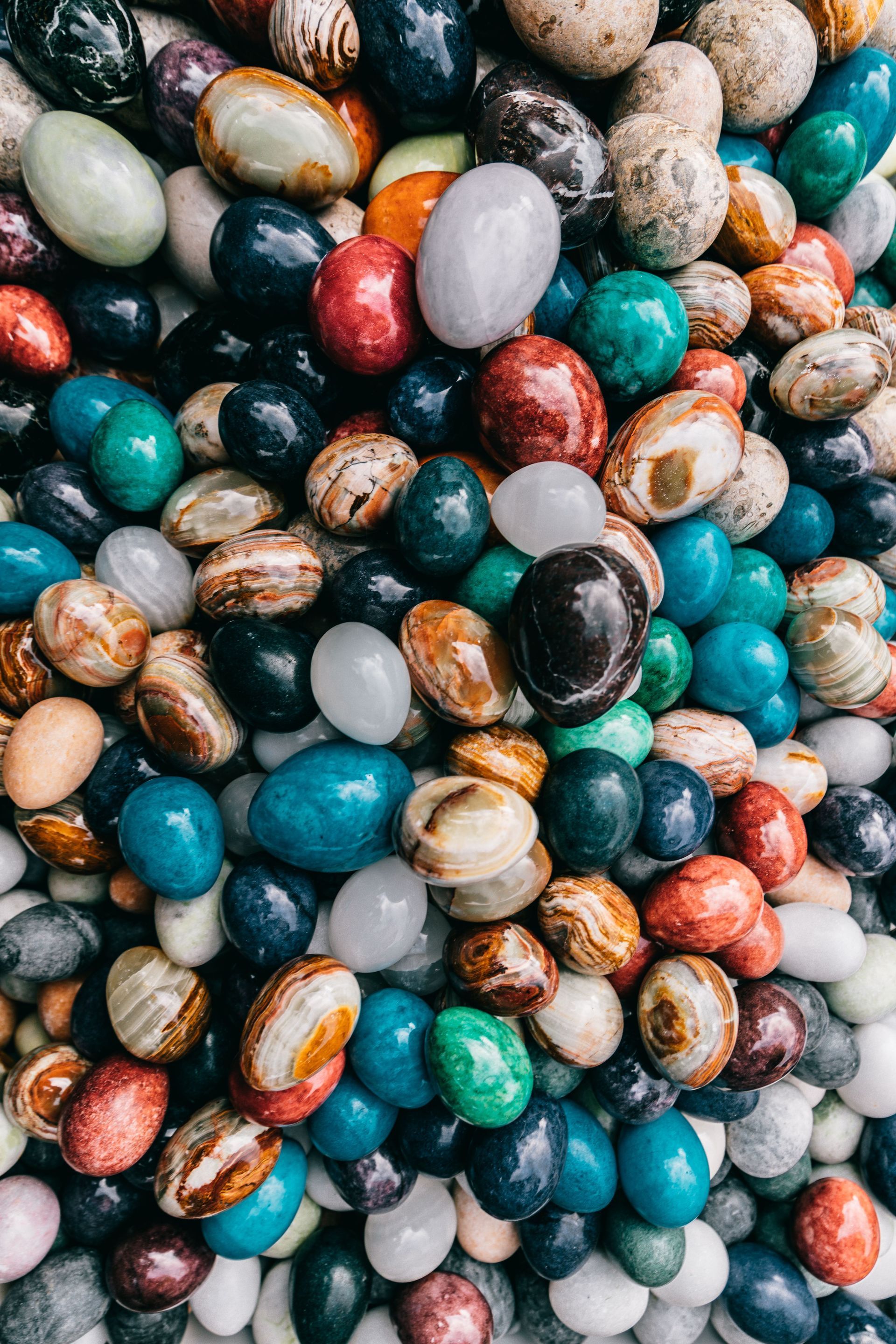 Close-up of a pile of colorful polished stones and marbles in teal, gray, orange, and black.