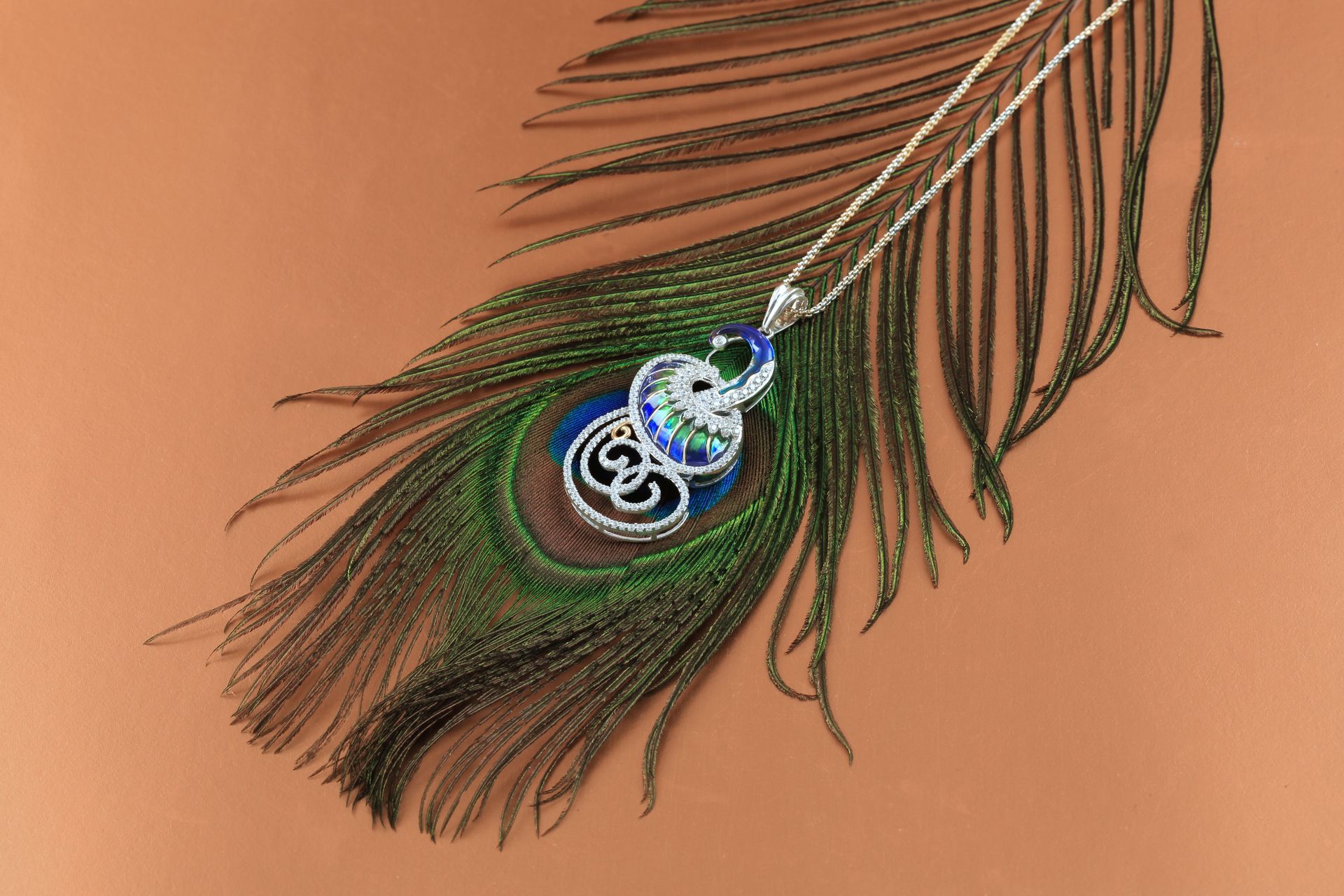 Peacock feather pendant necklace on tan skin, with blue and green details