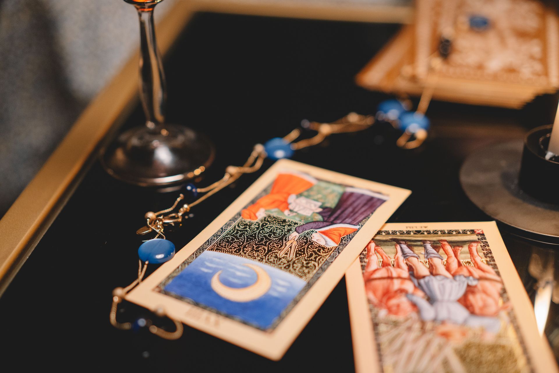 Tarot cards and blue beads arranged on a black table beside a candle holder