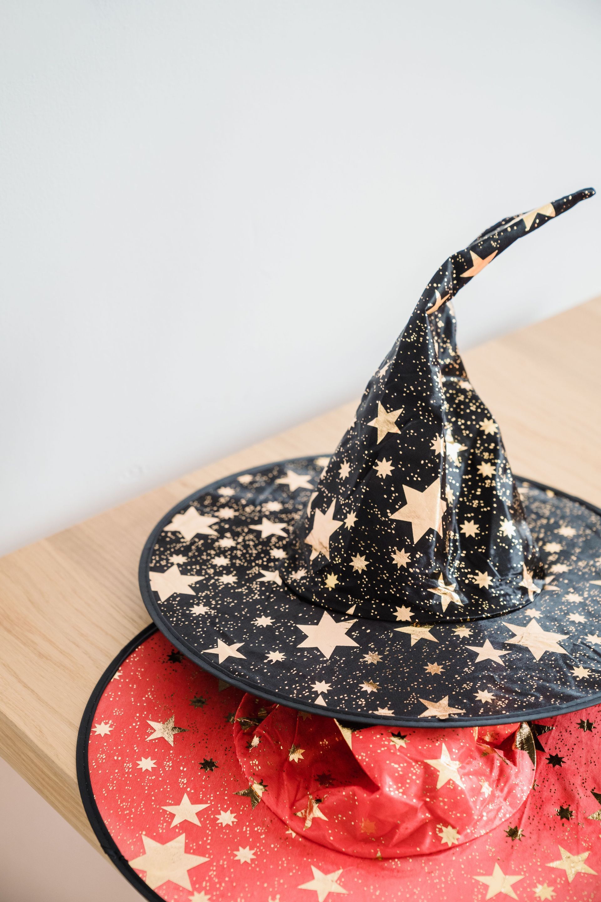 Two stacked star-patterned witch hats, black on red, on a wooden surface
