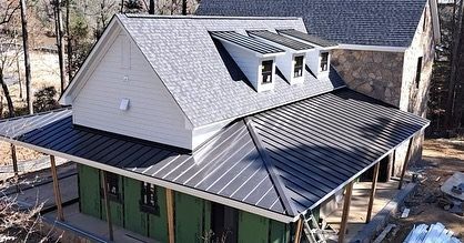 House with black metal roof, white siding, and dormer windows under construction.