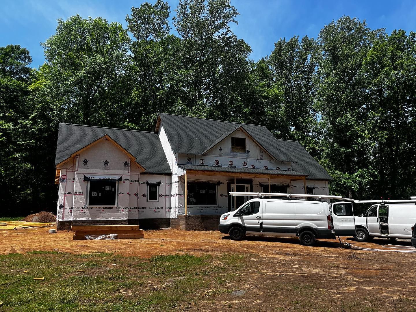 new construction roofing near me A house under construction with white vans parked in front. Brown dirt and green trees in the background.