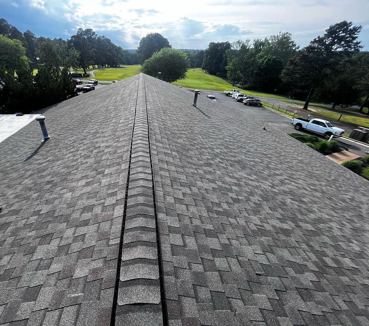 View of a shingled roof from above, with a center ridge line and a park in the background.
