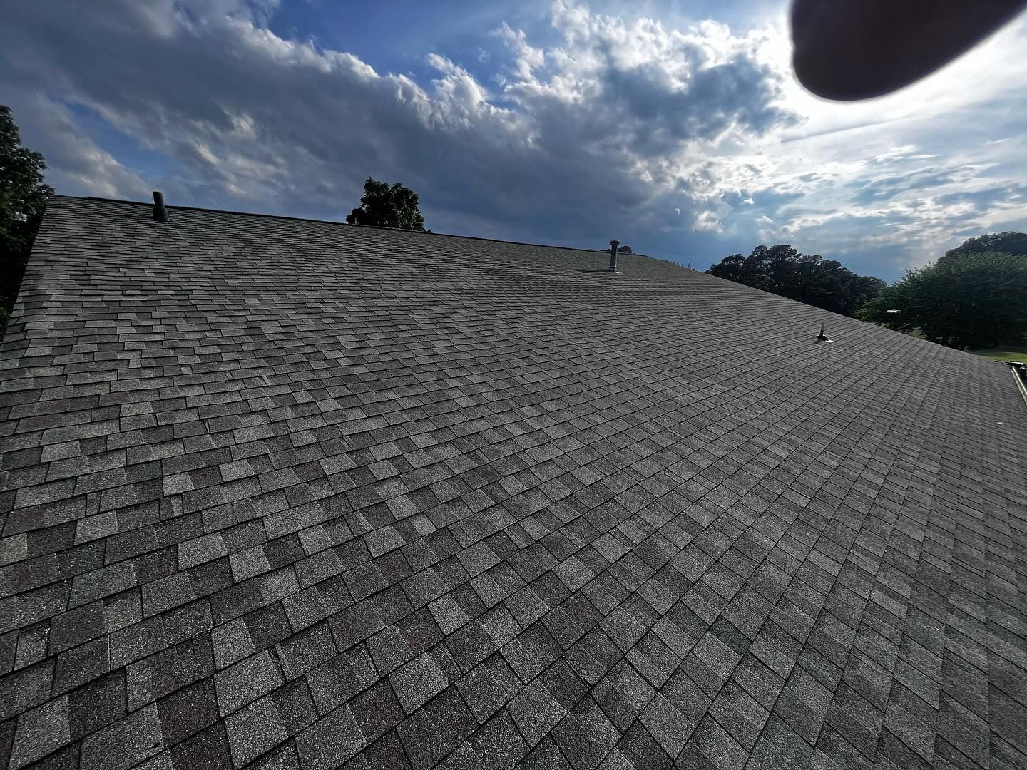 Gray asphalt shingle roof under a cloudy blue sky.