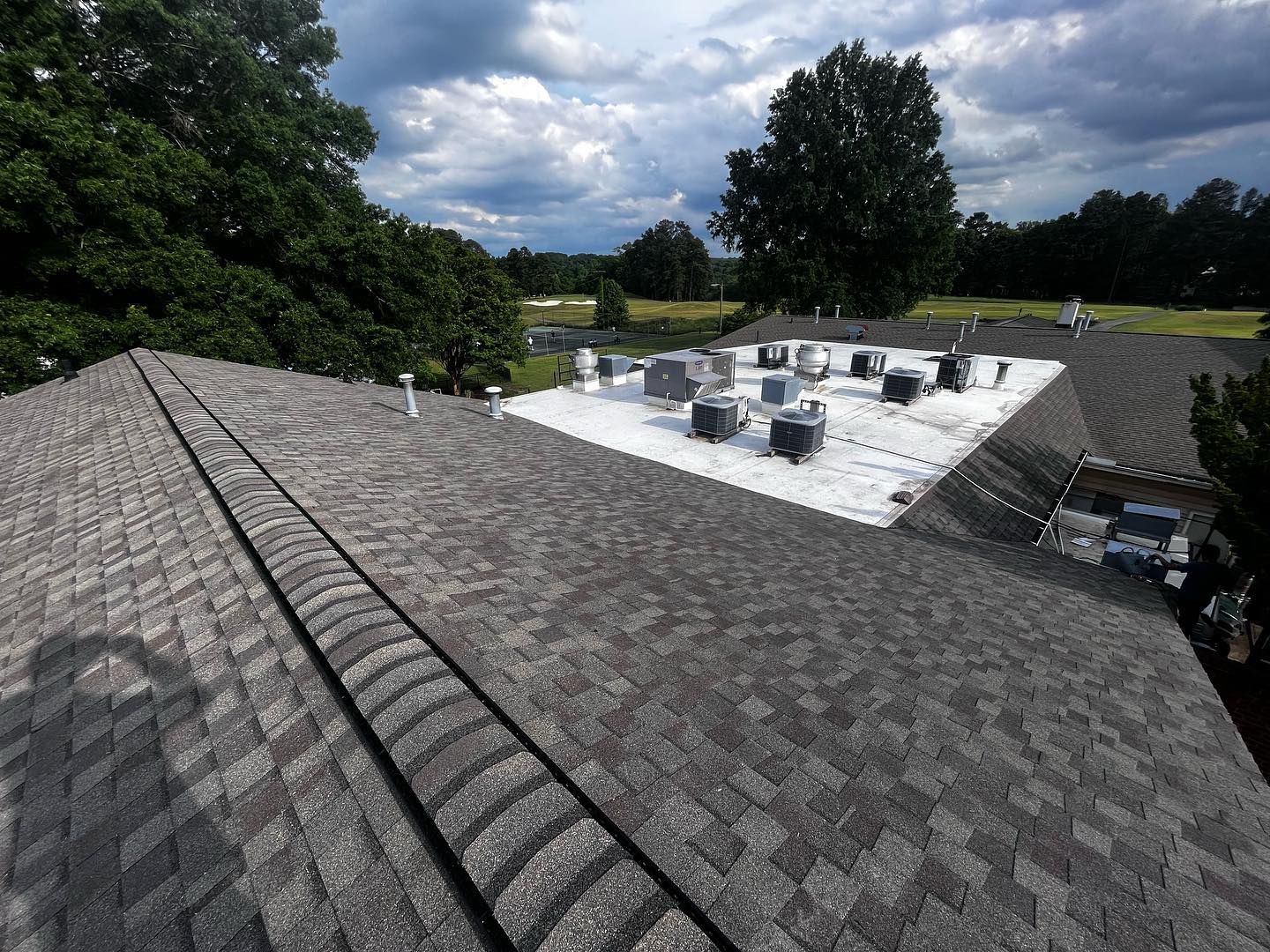 commercial roofing mechanicsville va Gray shingled roof with white flat roof section holding HVAC units, trees, and a golf course in the background.