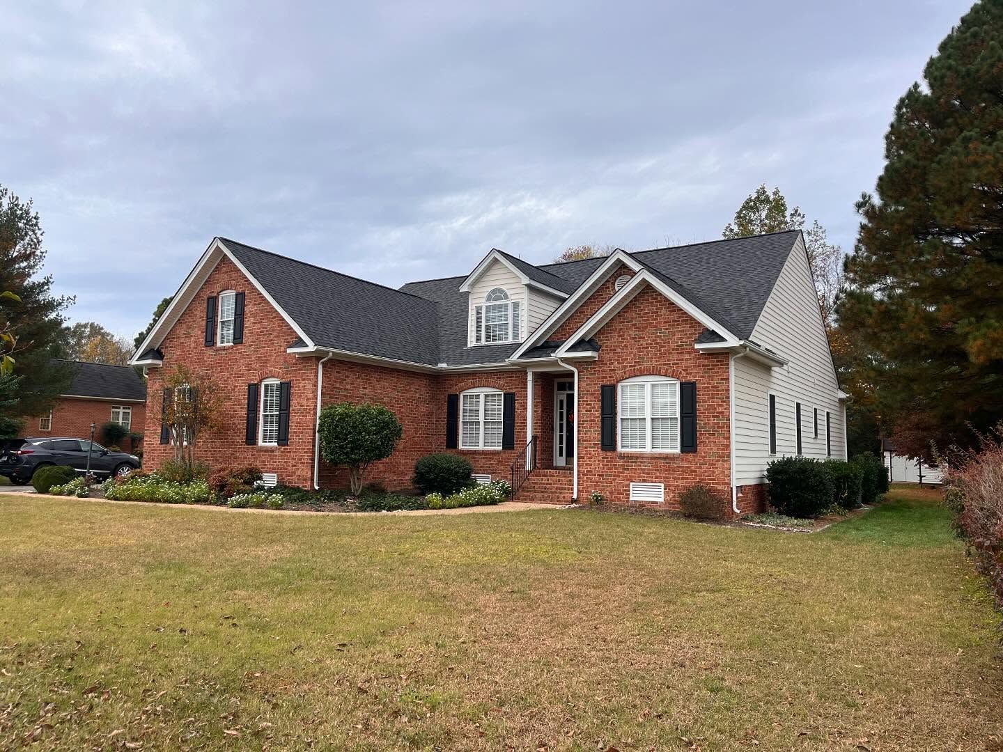 Brick house with black shutters and dark roof on a cloudy day.
