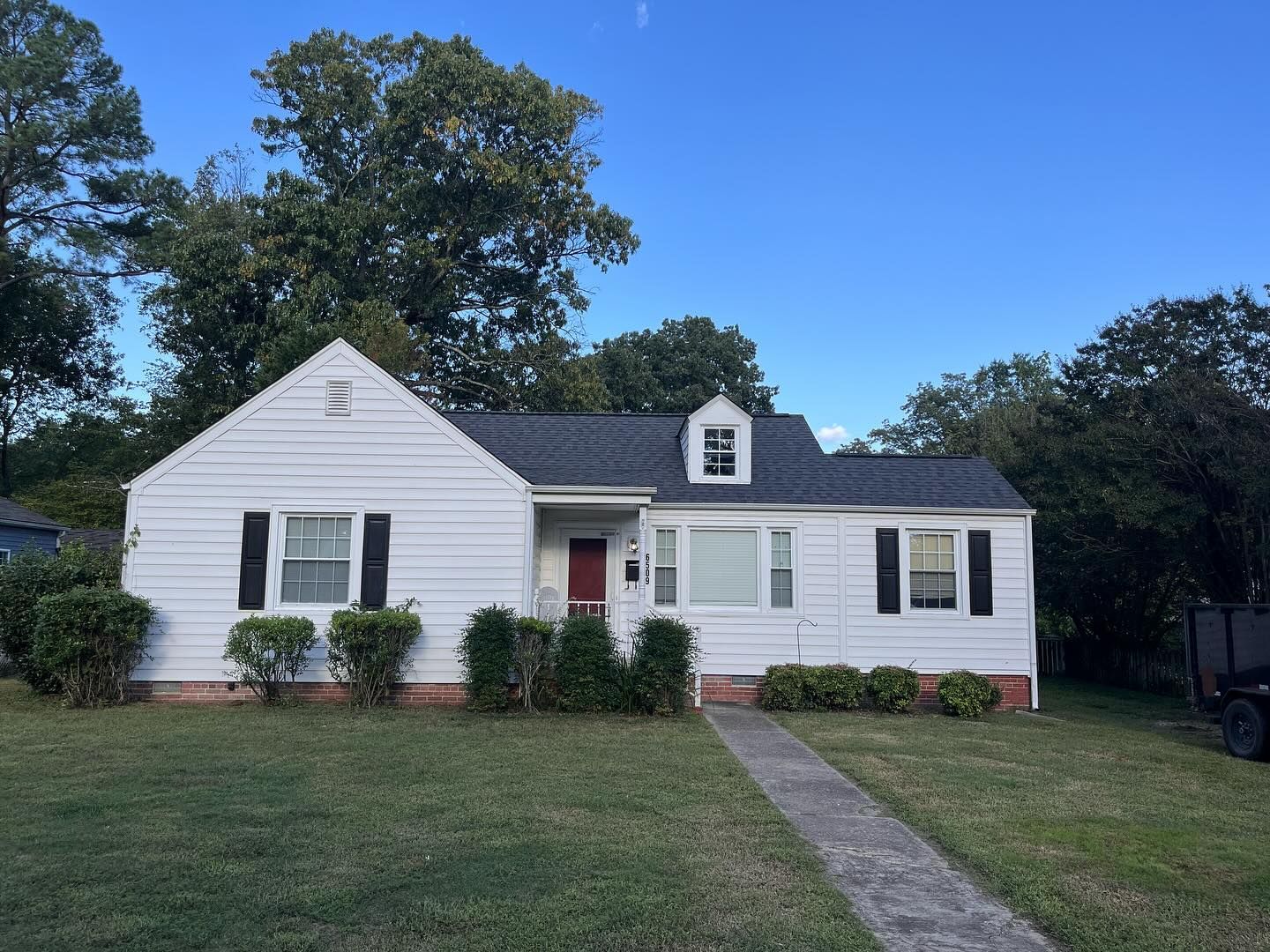White bungalow with a dark roof and black shutters, standing in front of a green lawn.