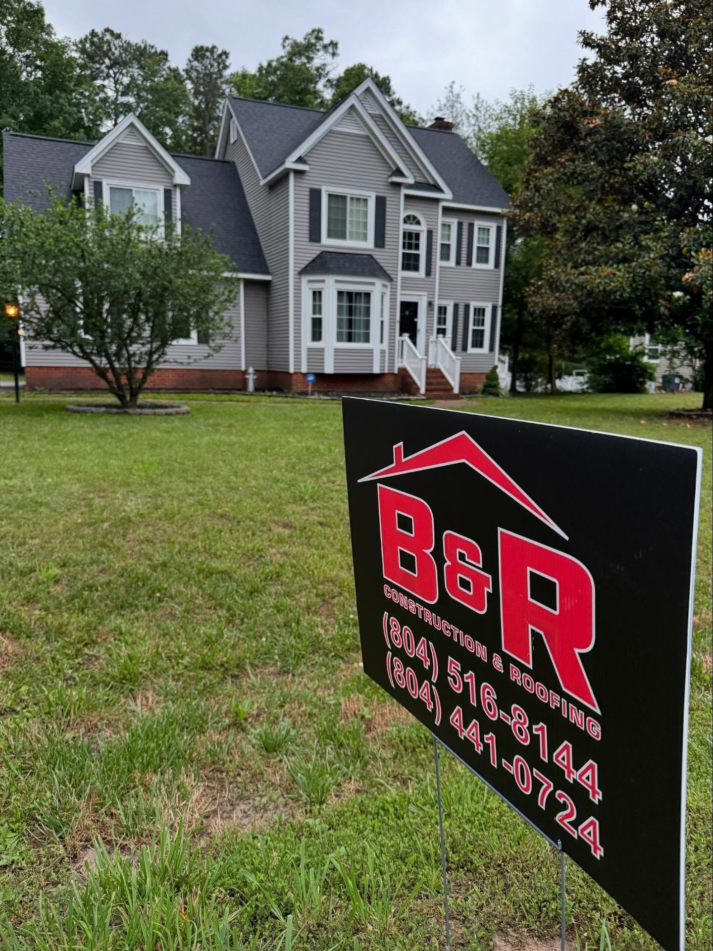 Gray house with B&R Construction sign in front. Green lawn, overcast sky.
