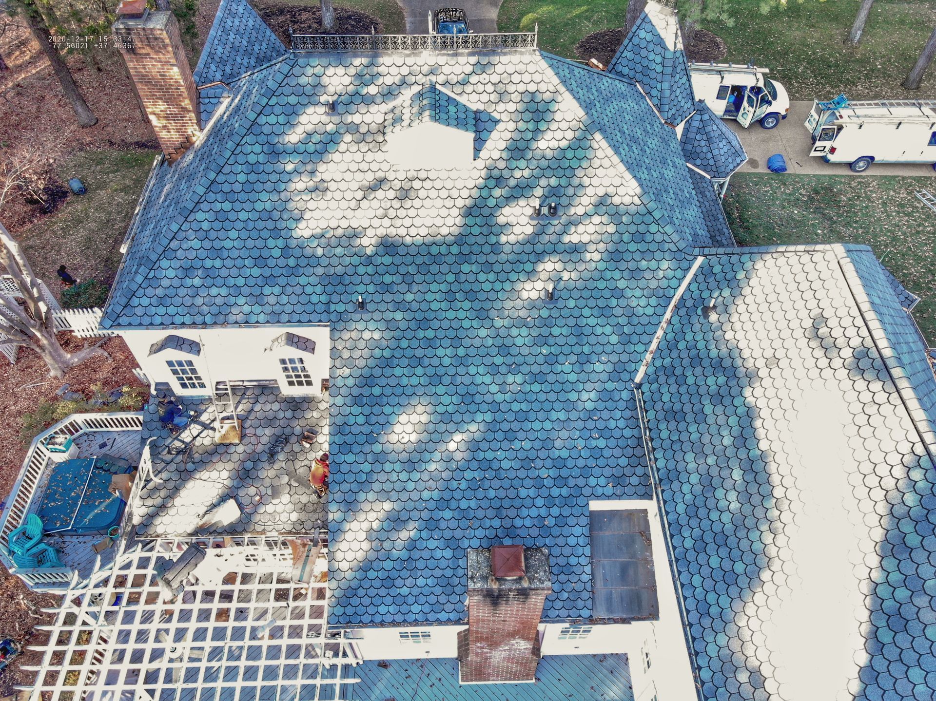 Overhead view of a house with a blue roof and several service vehicles in the yard.