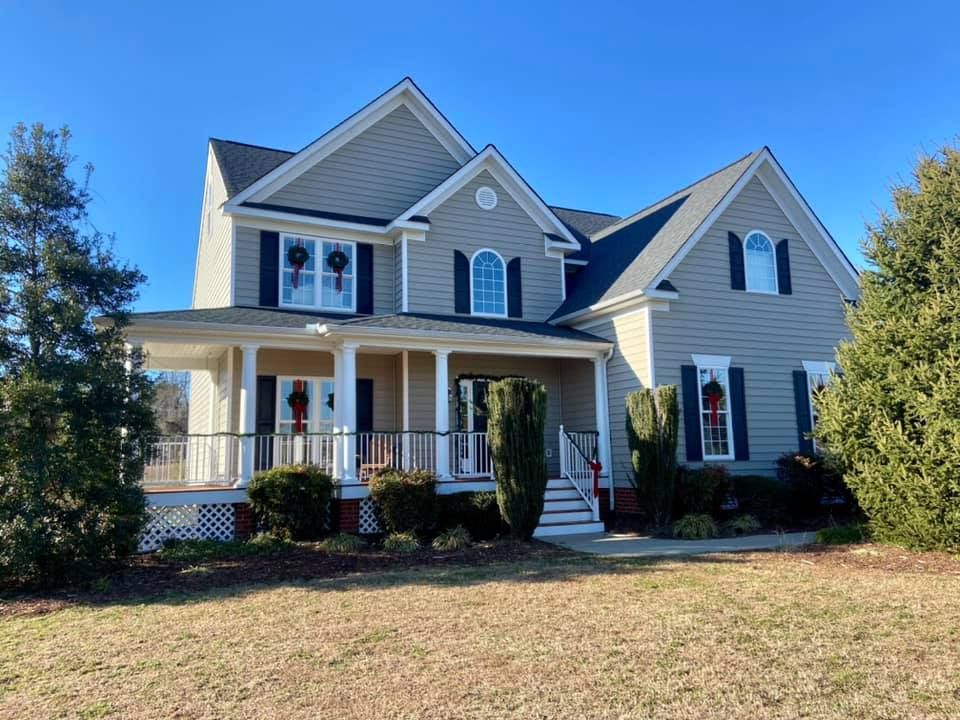 Two-story house with gray siding, black shutters, and a front porch, on a sunny day.