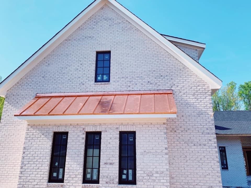 White brick house with copper awning, black windows, and a clear blue sky.