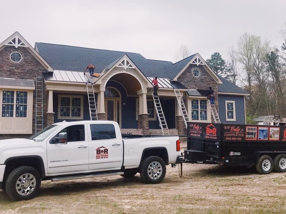 White truck and trailer with roofing workers on a blue house, installing a roof.