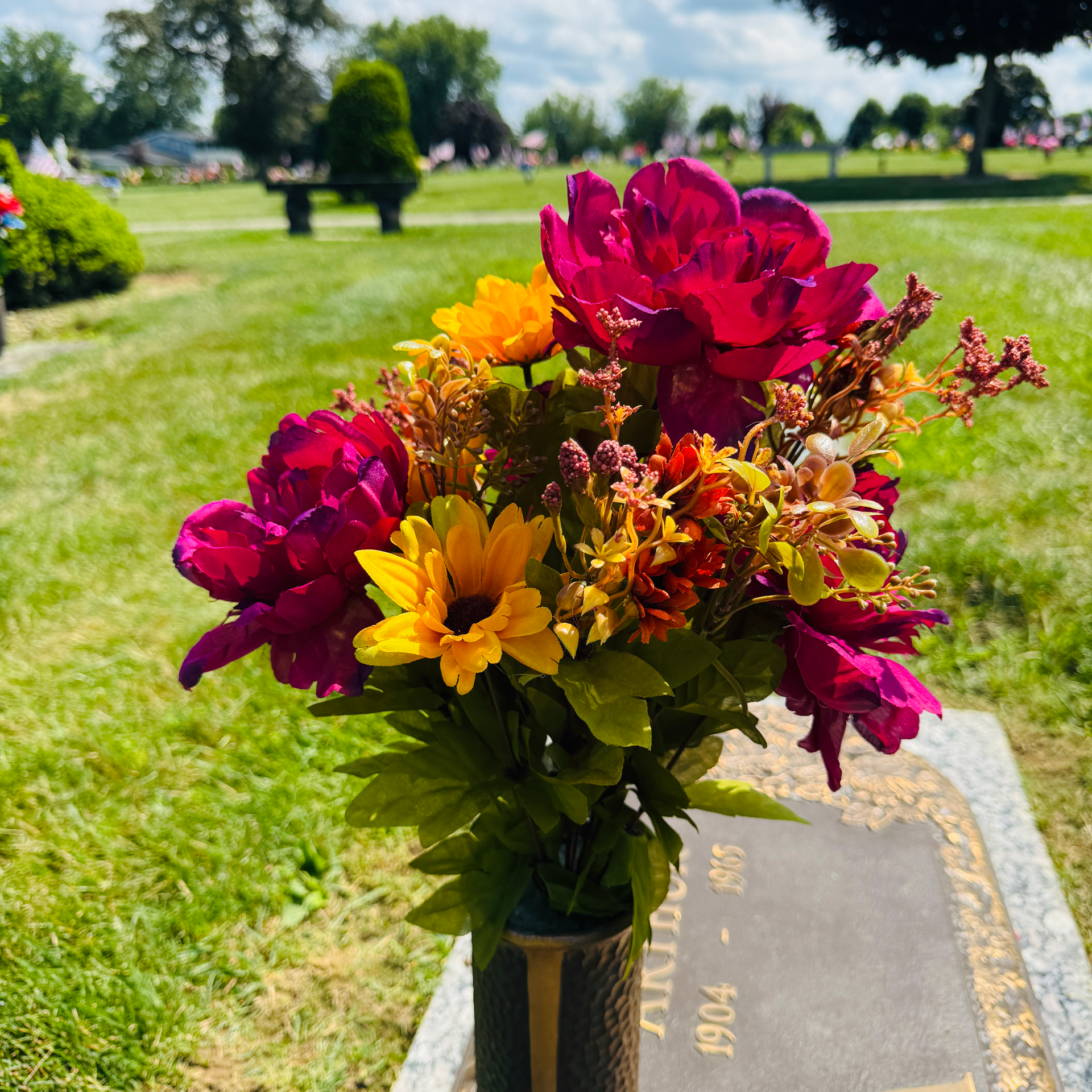 Colorful flowers in a vase on a cemetery grave marker outdoors. Reddish pink, yellow