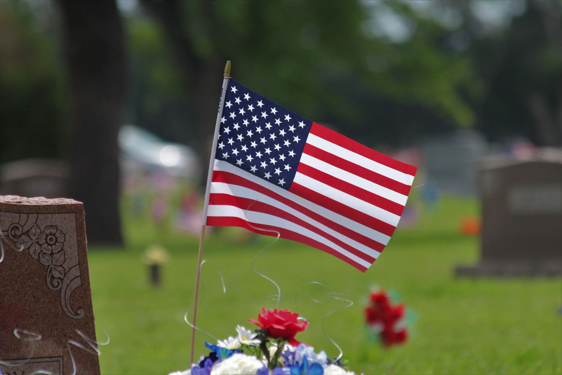 American flag on a gravesite with red and blue flowers in a cemetery