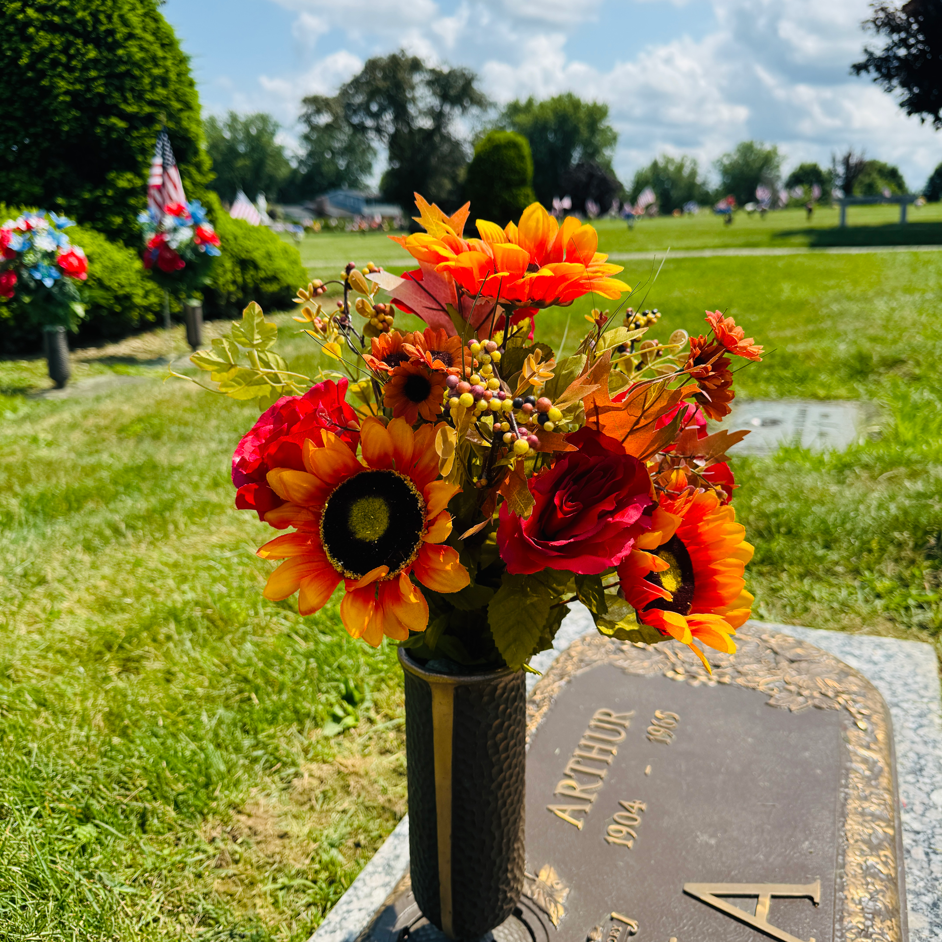Colorful flowers in a vase on a cemetery grave marker outdoors. yellow, orange, red