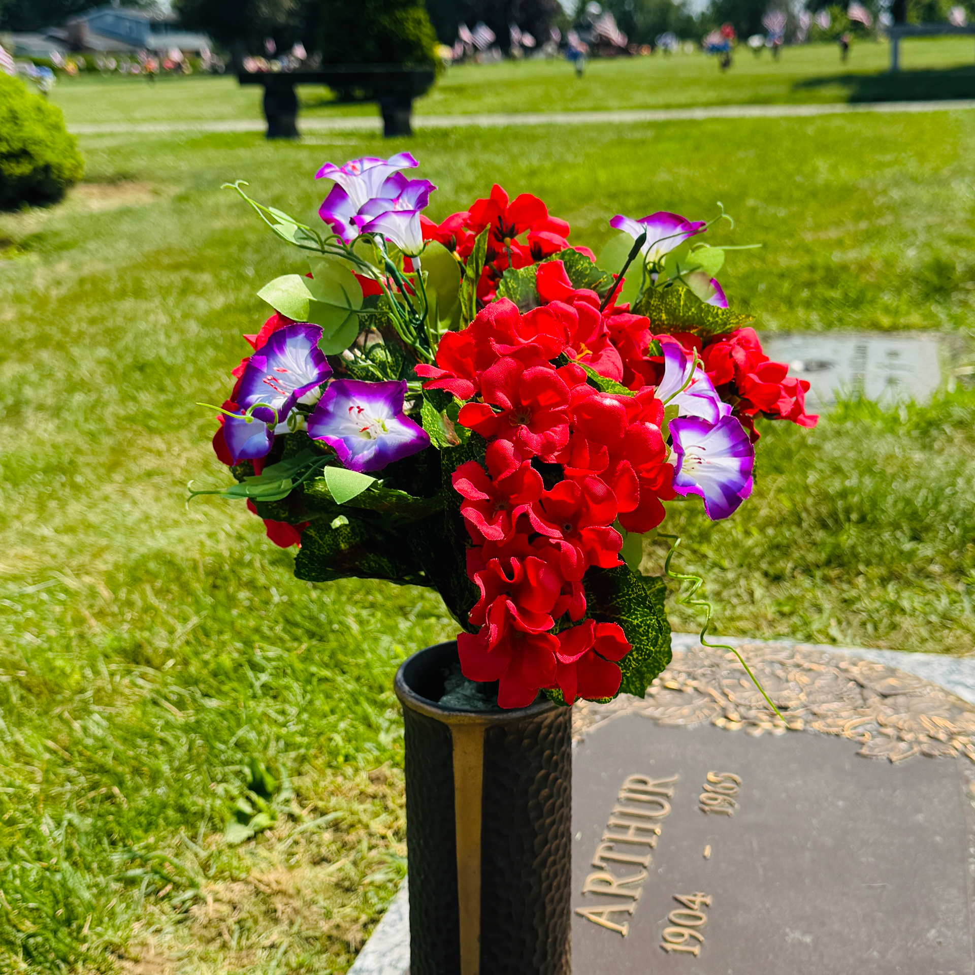 Colorful flowers in a vase on a cemetery grave marker outdoors. red, white, purple