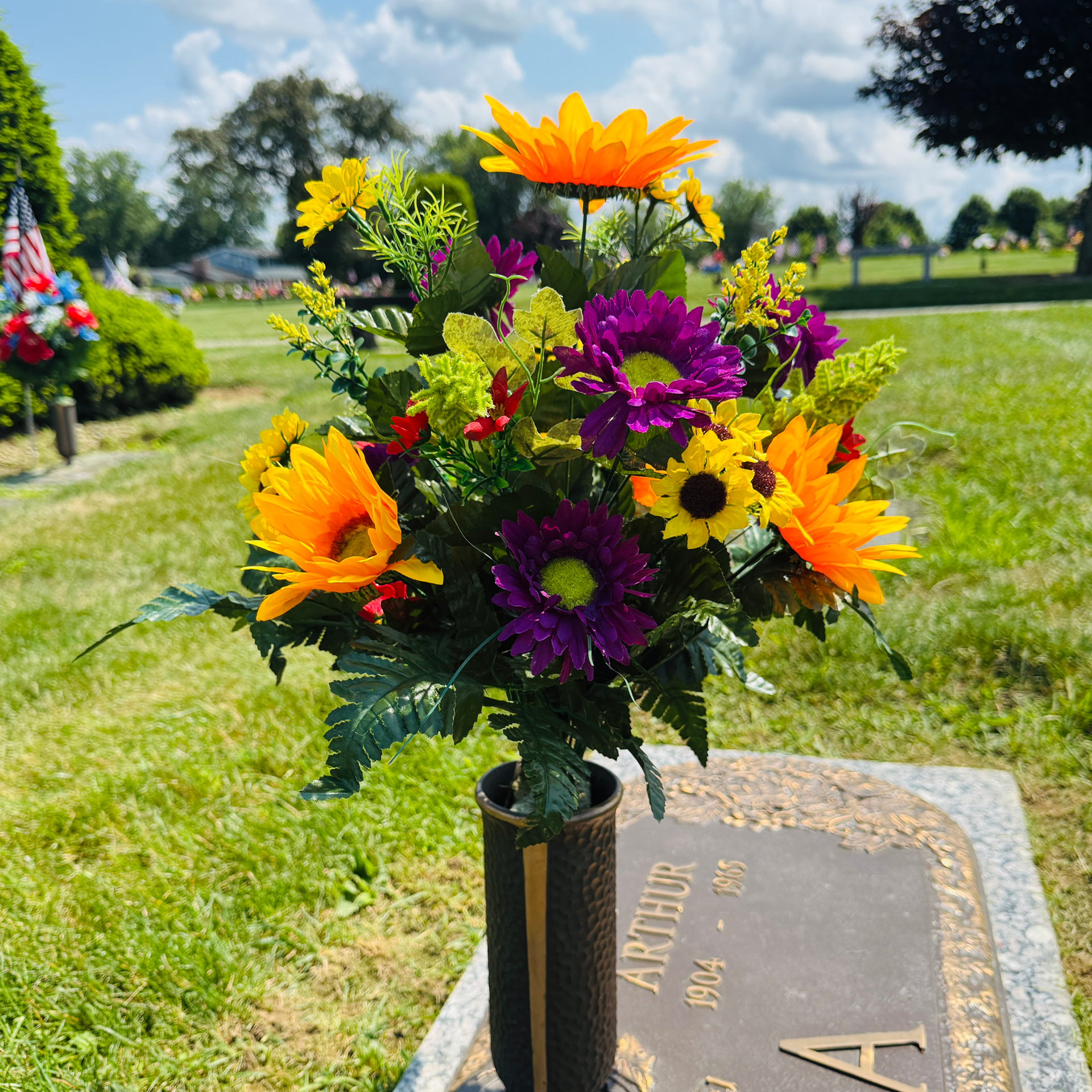 Colorful flowers in a vase on a cemetery grave marker outdoors. yellow, purple, and green