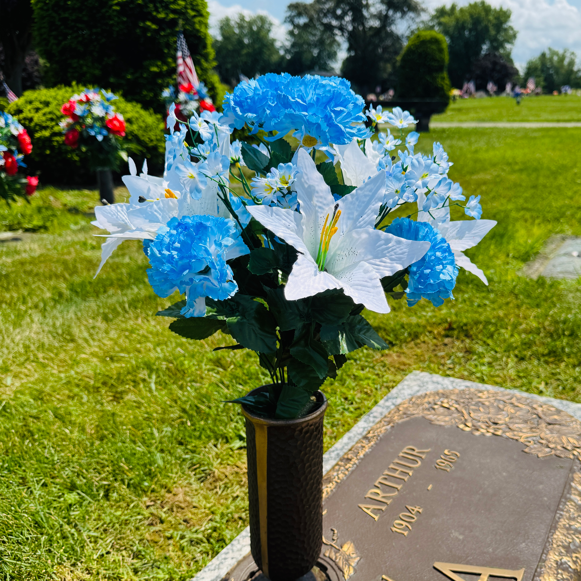 Colorful flowers in a vase on a cemetery grave marker outdoors. bright blue, light blue