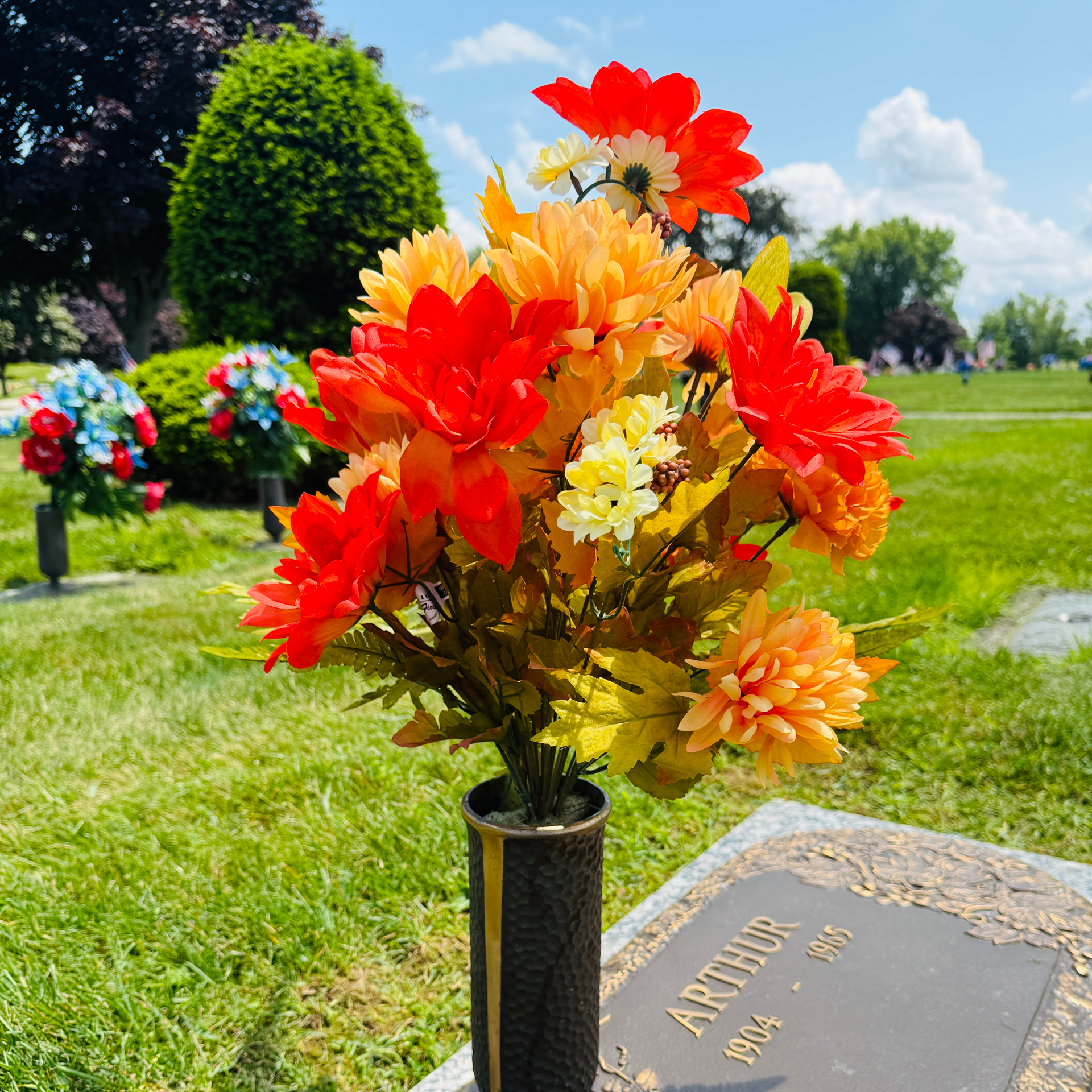 Colorful flowers in a vase on a cemetery grave marker outdoors. yellow, orange, white