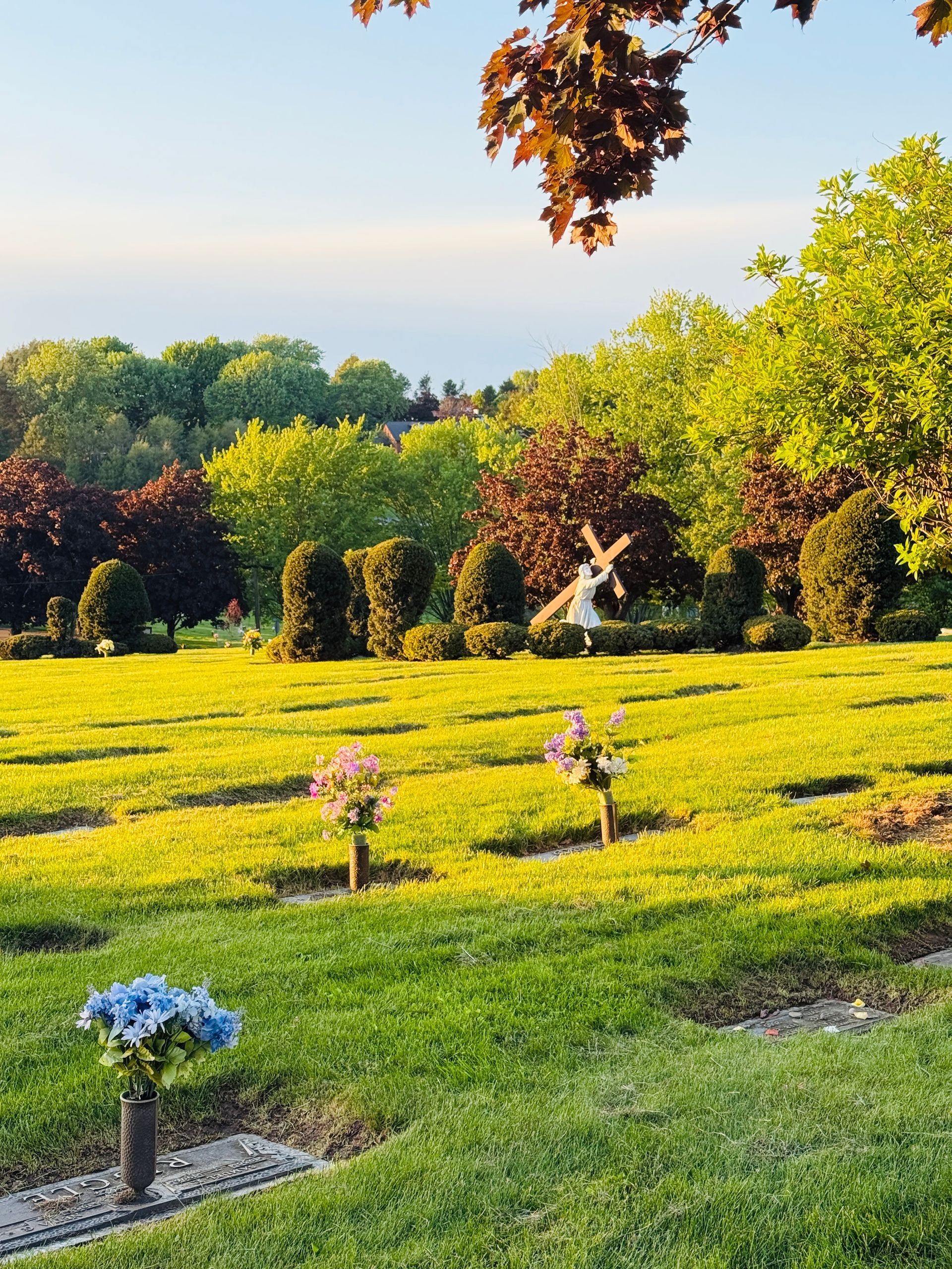 Sunny garden with green lawns, colorful flowers featuring a stone statue of christ carrying the cross