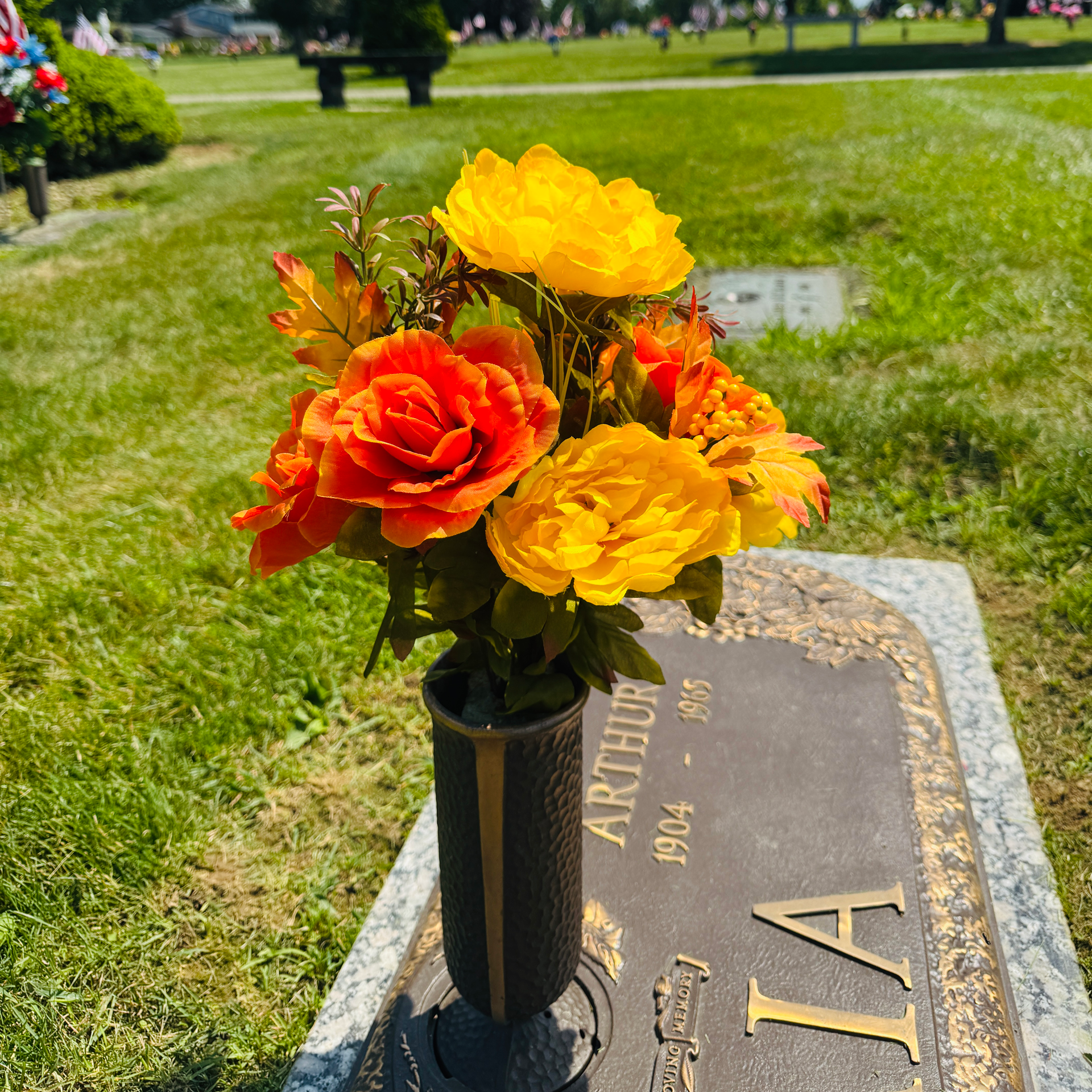 Colorful flowers in a vase on a cemetery grave marker outdoors. yellow and orange