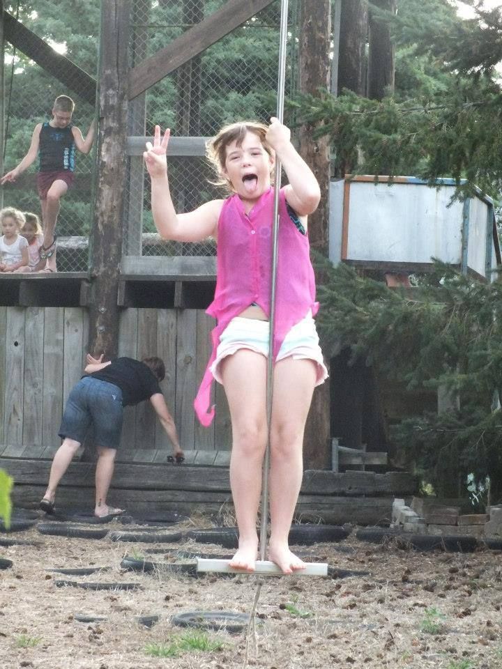 A girl in a pink shirt is standing on a pole giving a peace sign