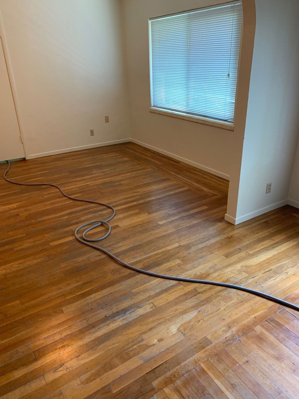 Wooden floor in a room with a window, wall, and cable.