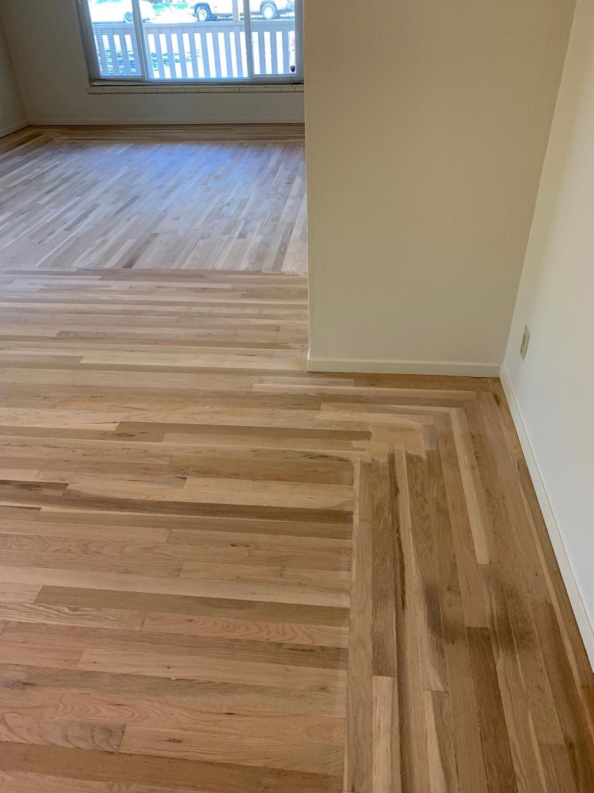 Hardwood flooring transitions from straight planks to a zig-zag pattern near a wall. Light wood tones dominate.