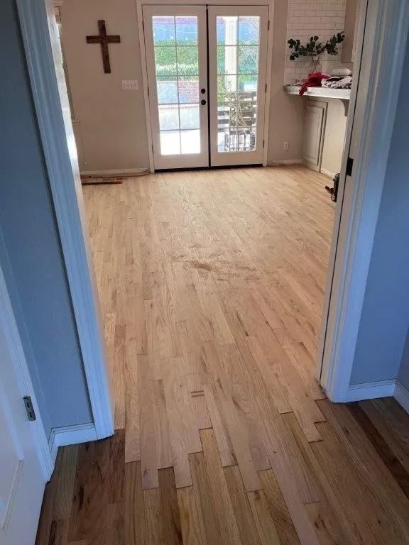 Hardwood floors in a home, transitioning from a darker to lighter color. French doors and a wall cross are visible.