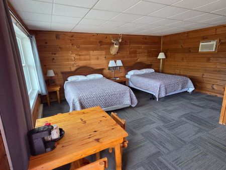 Cozy wood-paneled cabin bedroom with two beds, a warm lamp, and a small table on a carpeted floor