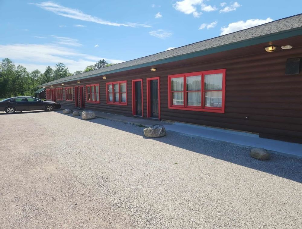Long brown building with red trim and windows beside a gravel lot under a blue sky