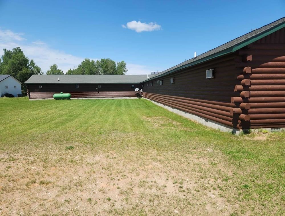 Grassy yard beside a long brown log cabin under a blue sky