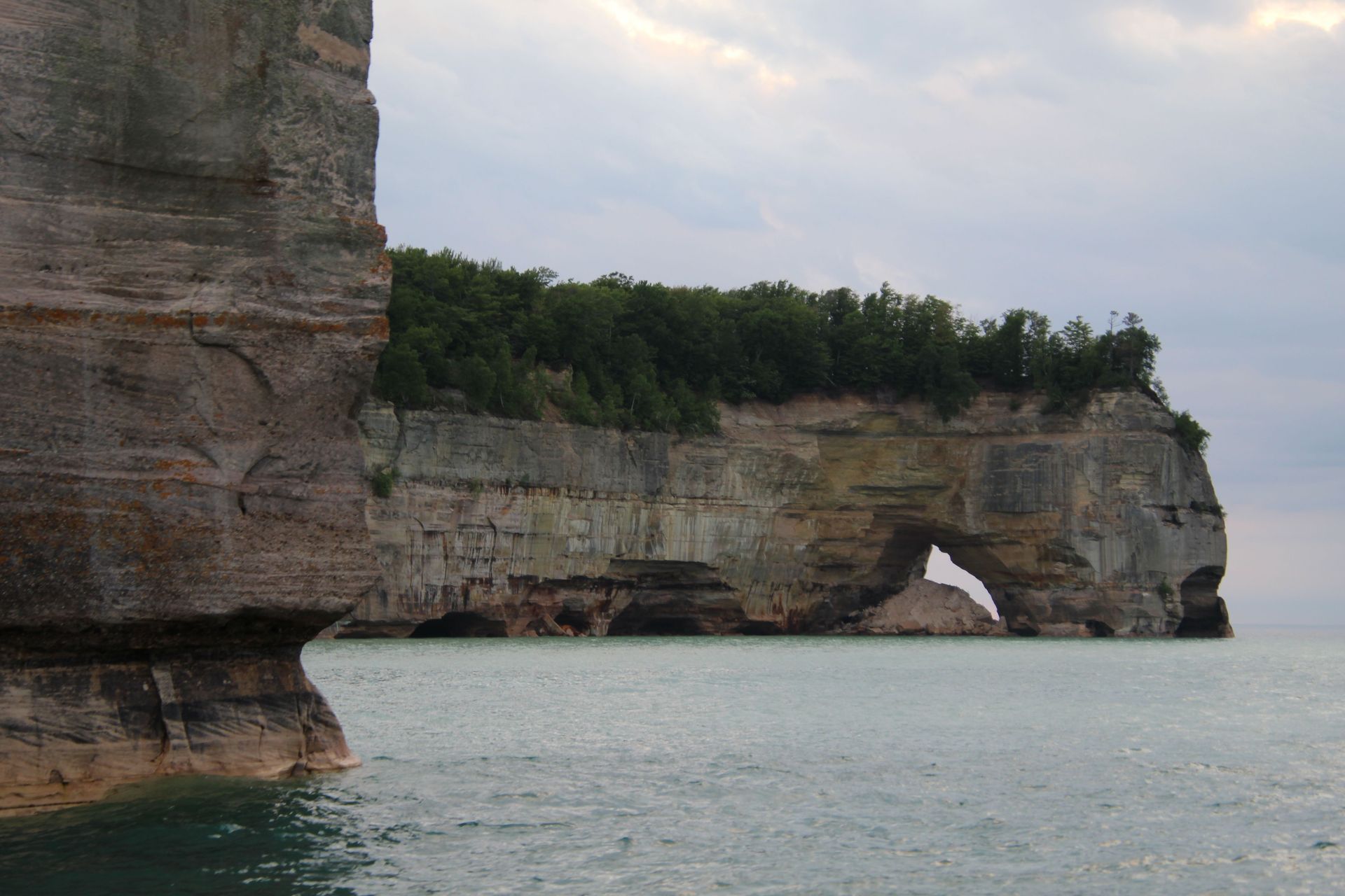 Rocky coastal cliffs with a sea arch over calm water under an overcast sky