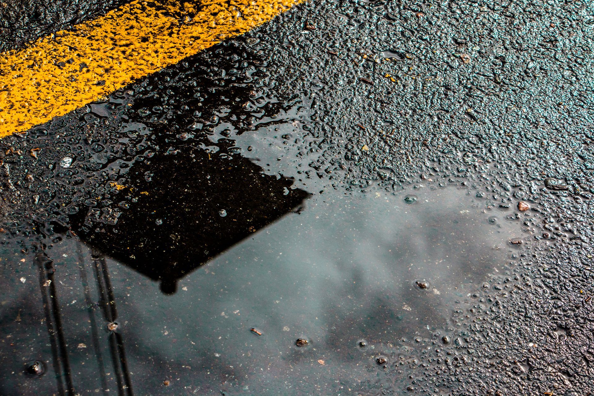 A puddle of water on the side of a road with a yellow line.