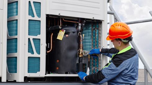 A man in a hard hat is working on an air conditioner.