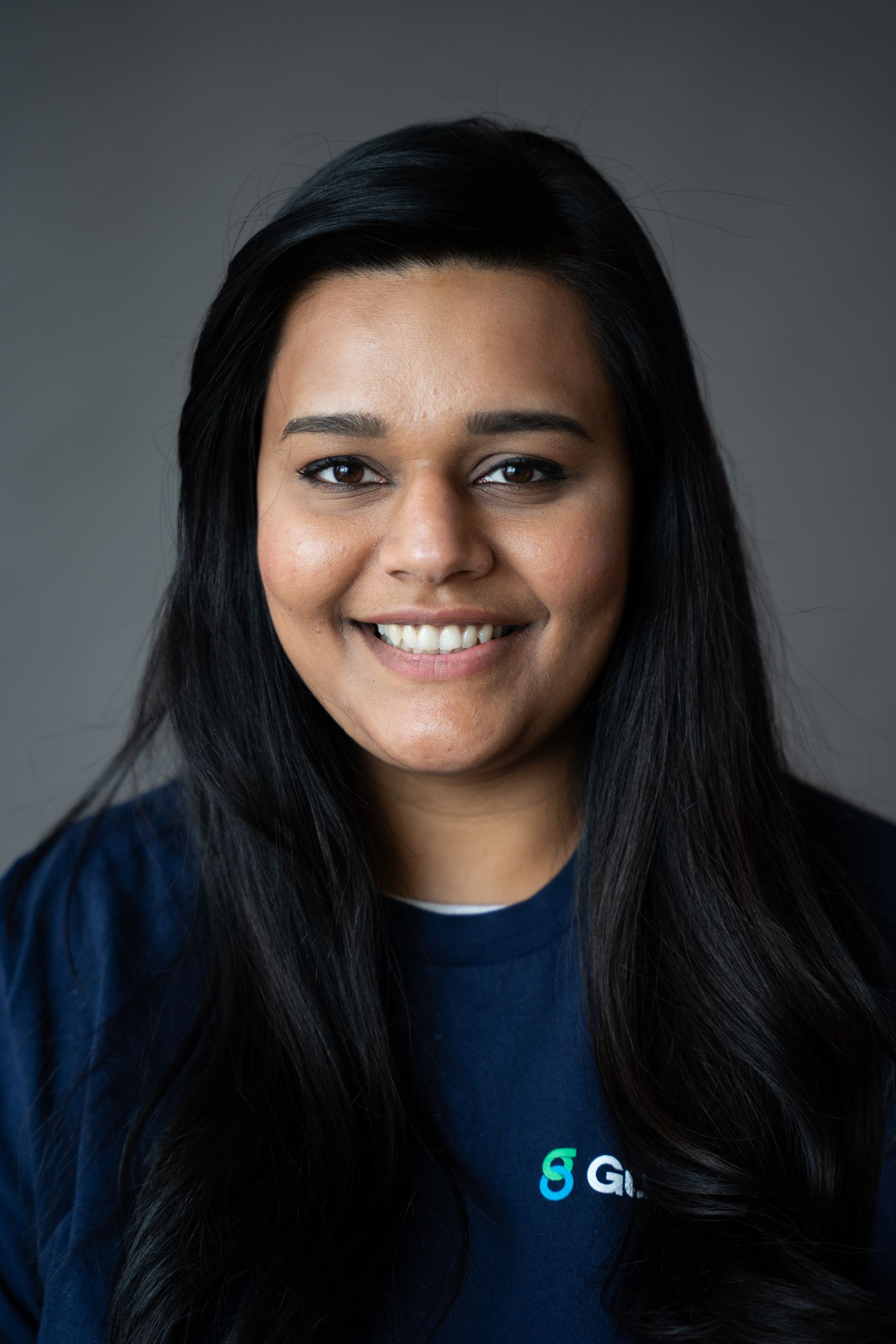 Smiling person with long dark hair in a navy shirt against a gray studio background