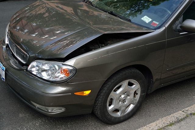 A car with a damaged hood is parked on the side of the road
