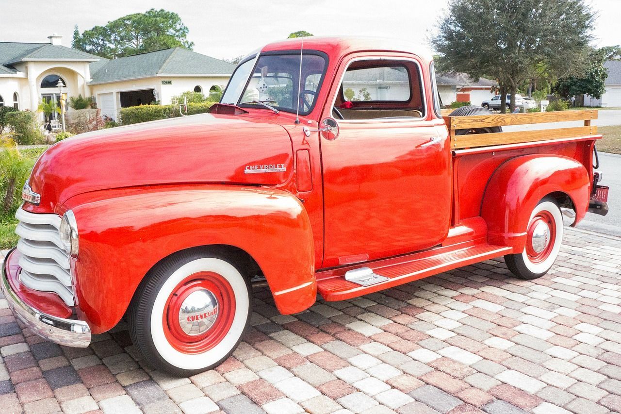 A red truck is parked on a brick driveway in front of a house.