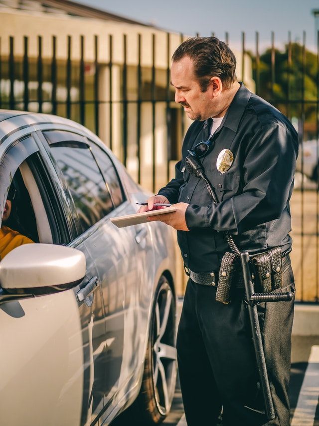 A police officer is writing a ticket to a man in a car.
