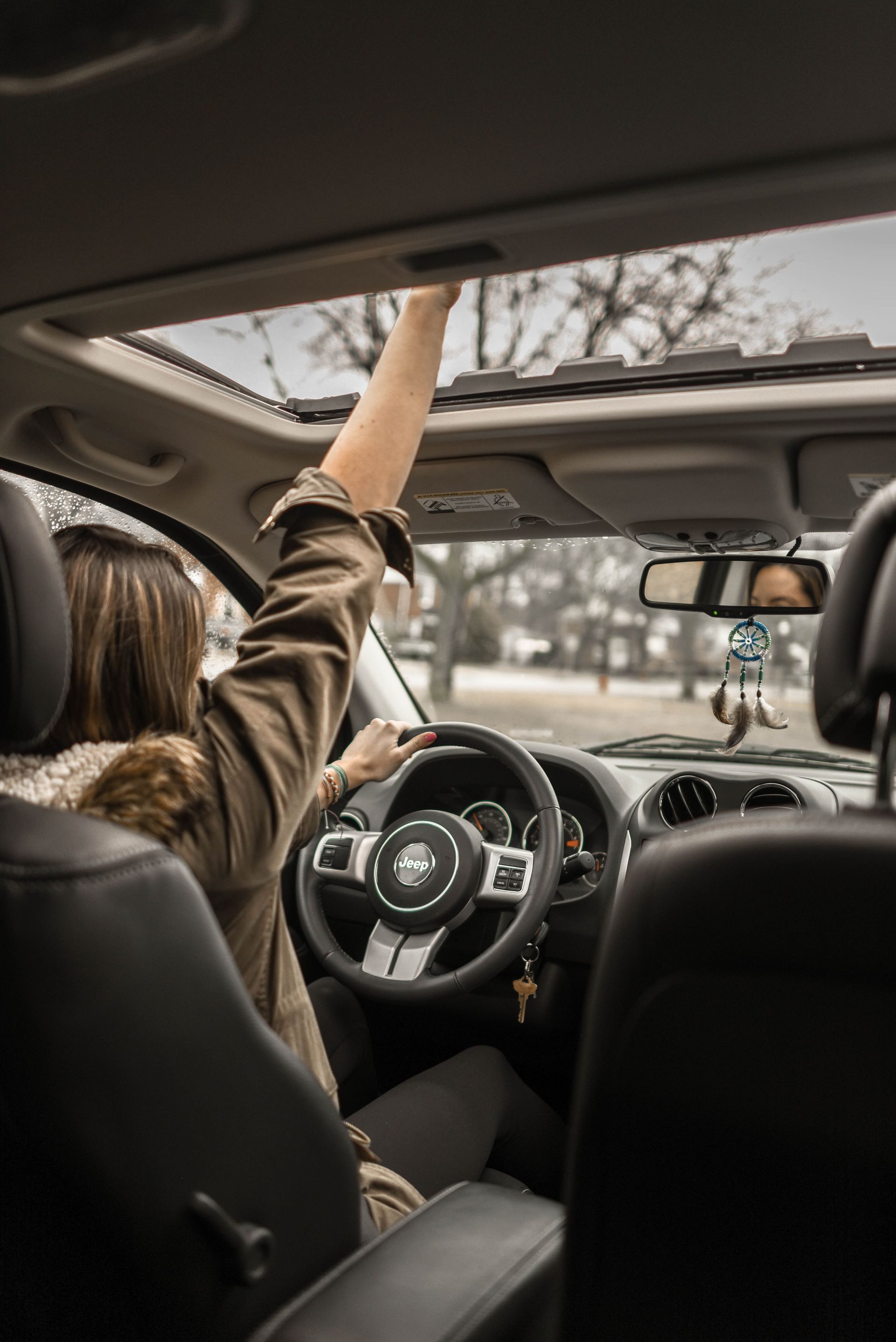 A woman is driving a car with her arms in the air.
