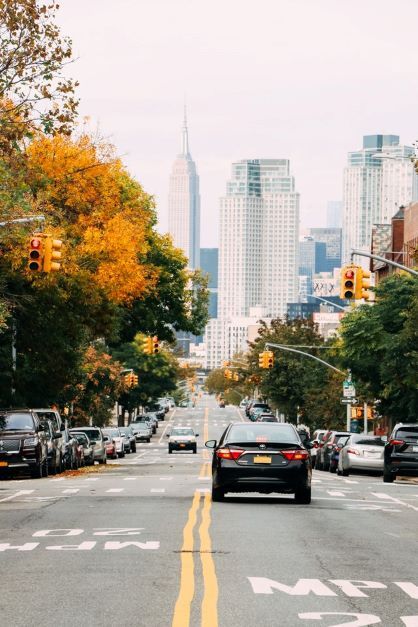 A car is driving down a city street with a skyline in the background.