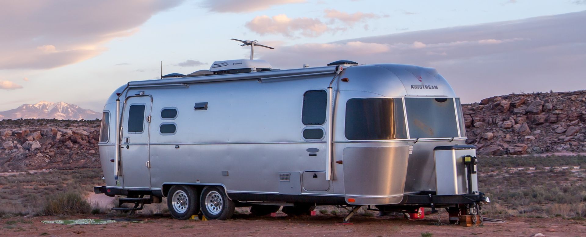 A silver airstream trailer is parked in the middle of a desert.