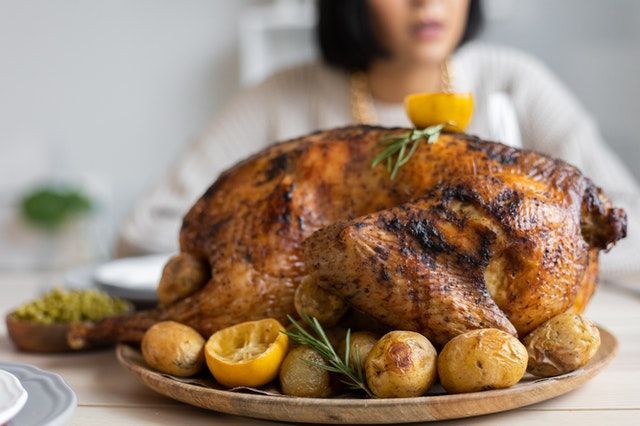 A woman is sitting at a table with a roasted turkey on a plate.