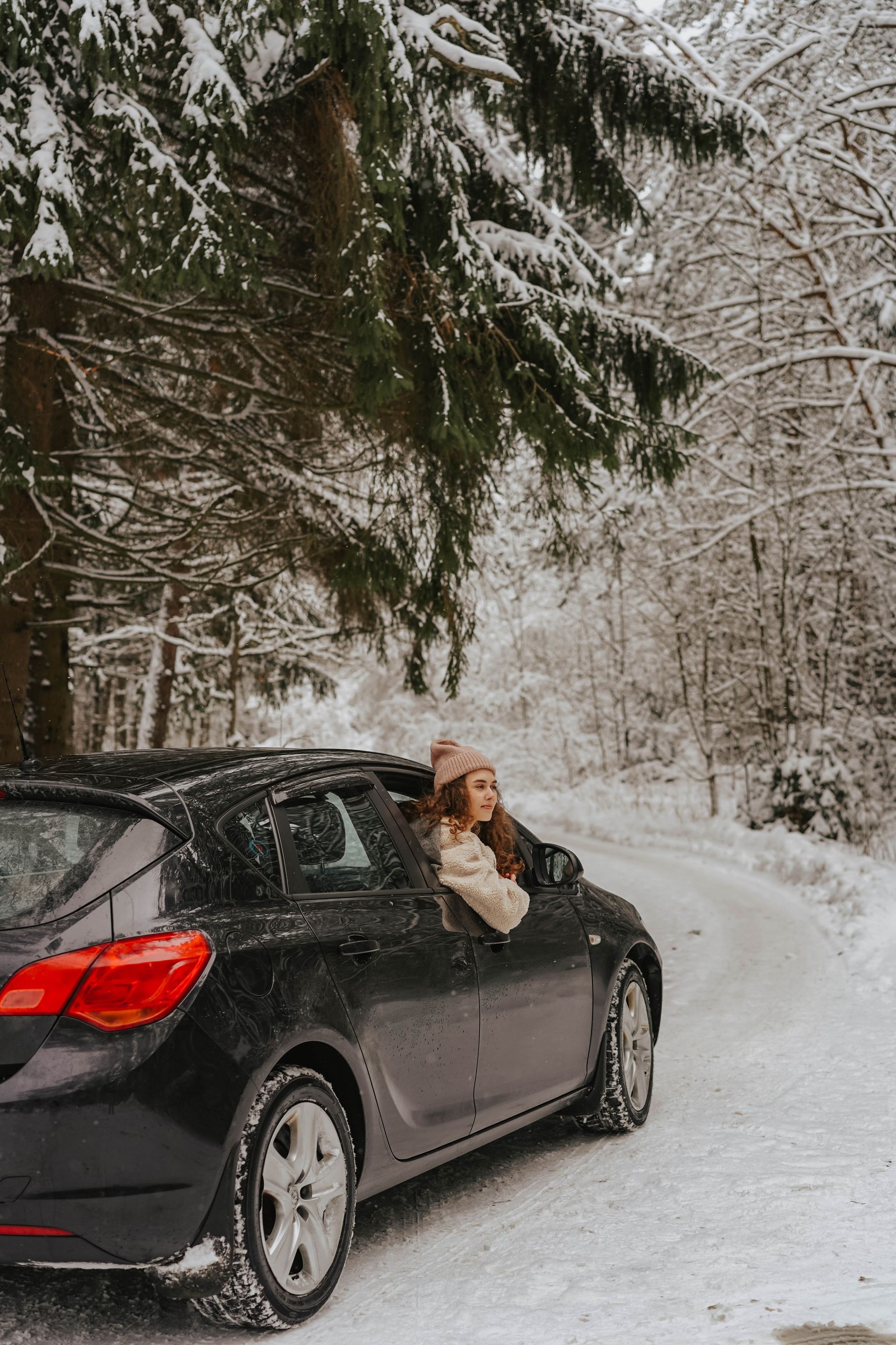 A woman is sitting in a car in the snow.